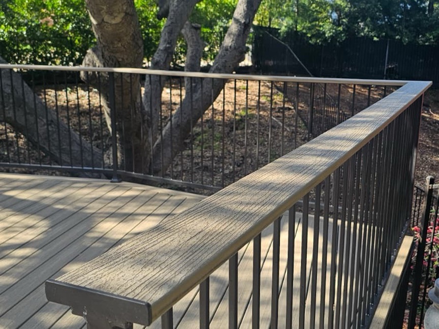 Composite deck detail with a wood-grain top rail and black metal balusters