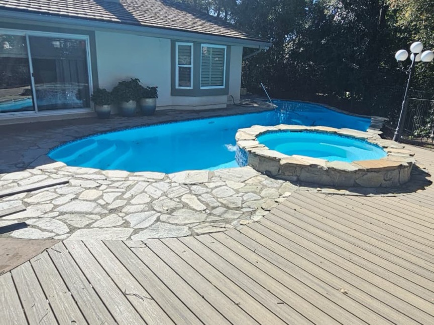 Pool surround with a raised natural-stone spa and adjacent composite deck